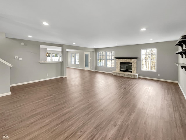 unfurnished living room featuring a healthy amount of sunlight, a fireplace, baseboards, and dark wood-type flooring