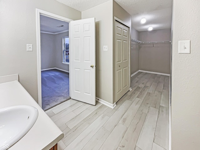 bathroom featuring a textured ceiling, wood finished floors, vanity, baseboards, and a spacious closet