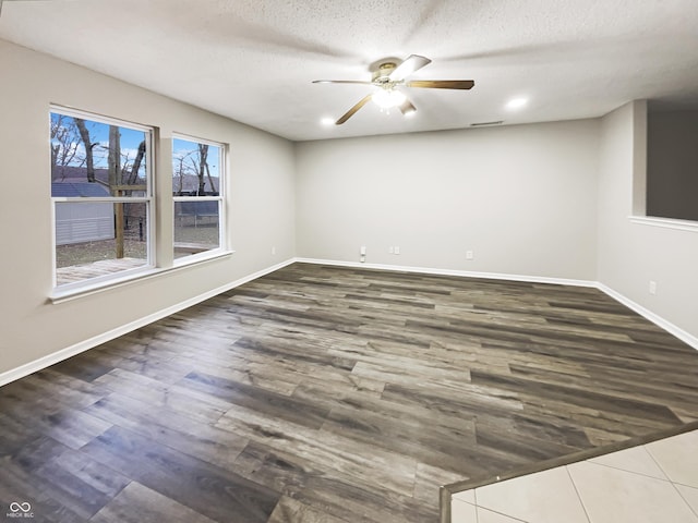 empty room with ceiling fan, a textured ceiling, baseboards, and wood finished floors