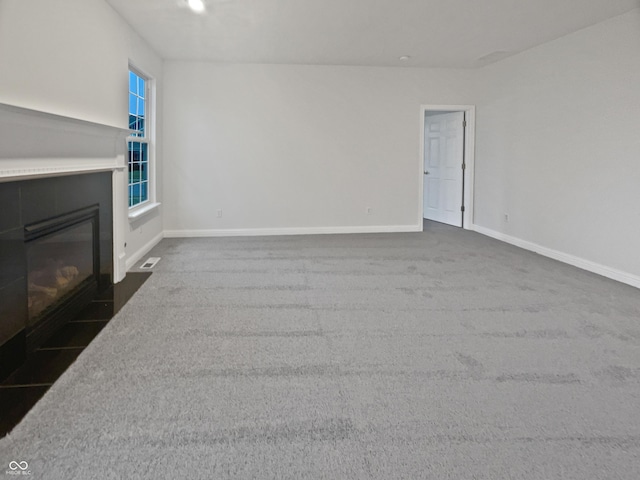 unfurnished living room with a fireplace with flush hearth, visible vents, baseboards, and dark colored carpet