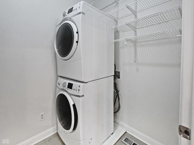 clothes washing area with laundry area, stacked washer and dryer, and baseboards