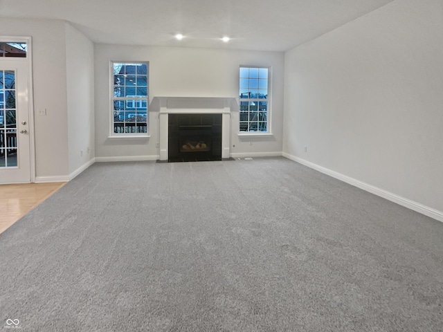 unfurnished living room with carpet floors, baseboards, and a tiled fireplace