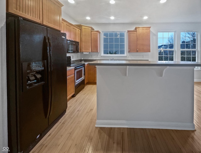 kitchen with recessed lighting, a kitchen island, black appliances, light wood finished floors, and a kitchen bar