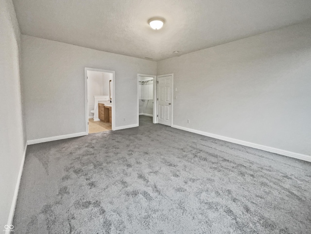 unfurnished bedroom featuring carpet, a walk in closet, ensuite bathroom, a textured ceiling, and baseboards