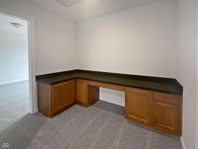 unfurnished office with carpet floors, built in study area, and visible vents