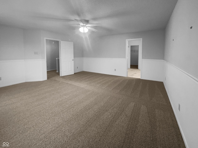 carpeted spare room featuring a textured ceiling, wainscoting, and a ceiling fan