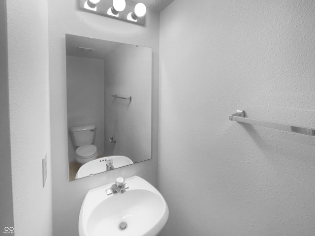 bathroom featuring toilet, a sink, and a textured wall