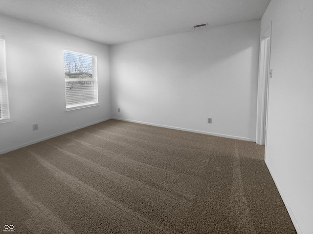 unfurnished room with a textured ceiling, carpet floors, visible vents, and baseboards