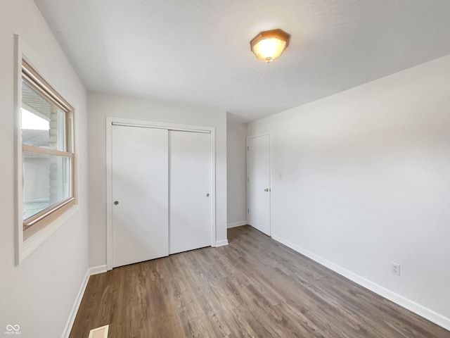 unfurnished bedroom with a closet, wood finished floors, visible vents, and baseboards