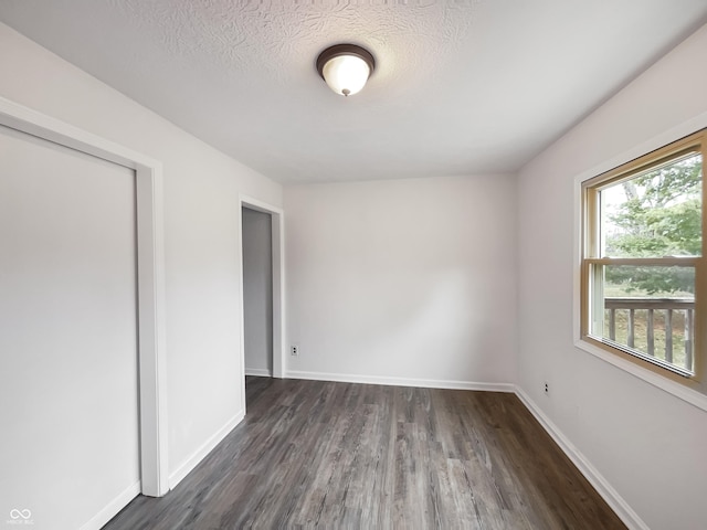 spare room featuring a textured ceiling, dark wood finished floors, and baseboards