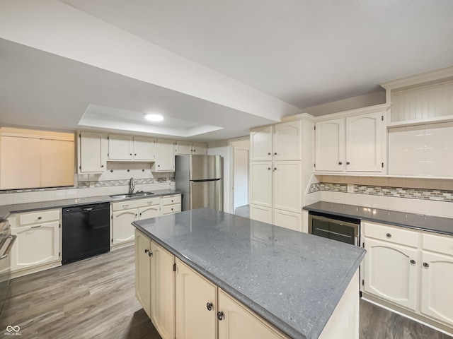 kitchen featuring a tray ceiling, tasteful backsplash, freestanding refrigerator, a sink, and dishwasher