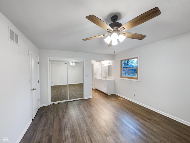 unfurnished bedroom with a ceiling fan, visible vents, baseboards, a closet, and dark wood finished floors