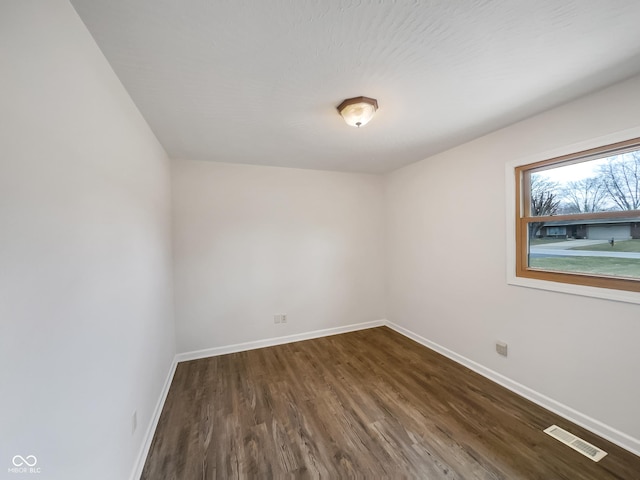 empty room featuring dark wood-style flooring, visible vents, and baseboards