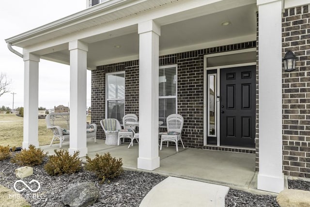 view of exterior entry featuring covered porch and brick siding