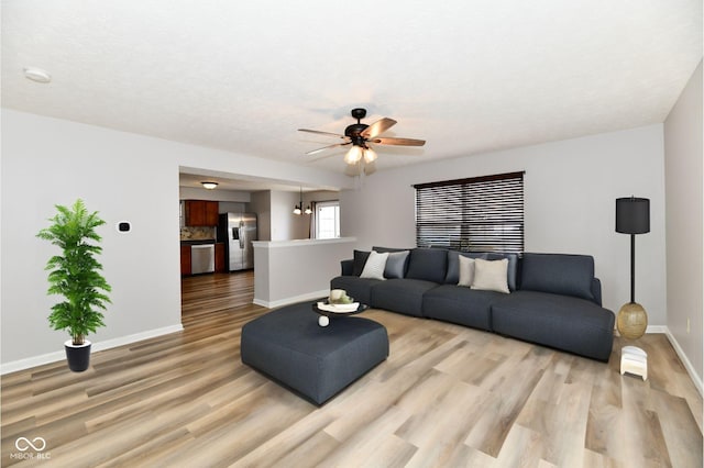 living area featuring ceiling fan with notable chandelier, light wood finished floors, and baseboards