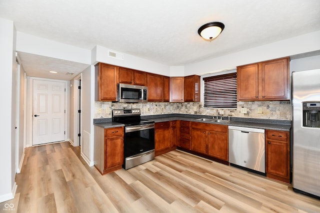 kitchen featuring stainless steel appliances, a sink, visible vents, light wood-style floors, and dark countertops