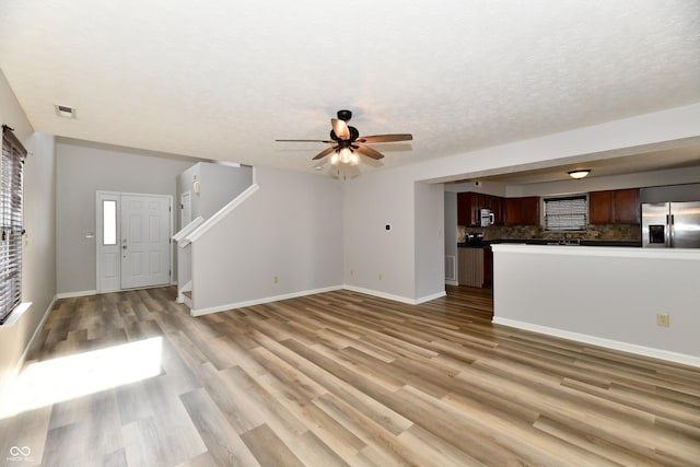 unfurnished living room with light wood-type flooring, stairway, baseboards, and a textured ceiling