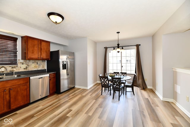 kitchen with tasteful backsplash, dark countertops, appliances with stainless steel finishes, a sink, and light wood-type flooring