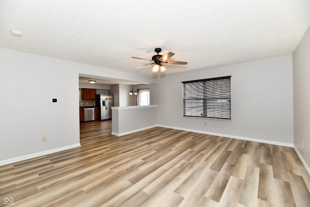 unfurnished living room featuring ceiling fan with notable chandelier, light wood-style flooring, and baseboards