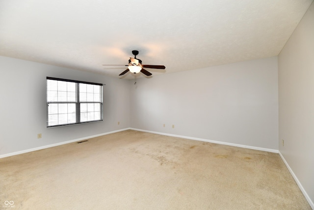 spare room with light carpet, visible vents, baseboards, and a ceiling fan