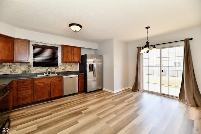 kitchen with light wood finished floors, tasteful backsplash, dark countertops, appliances with stainless steel finishes, and a sink