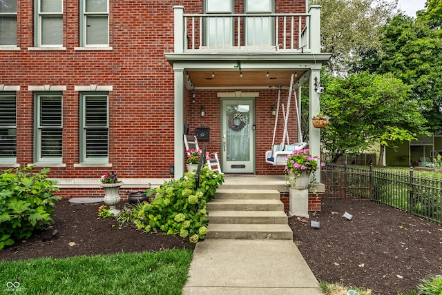 entrance to property featuring brick siding, fence, and a balcony