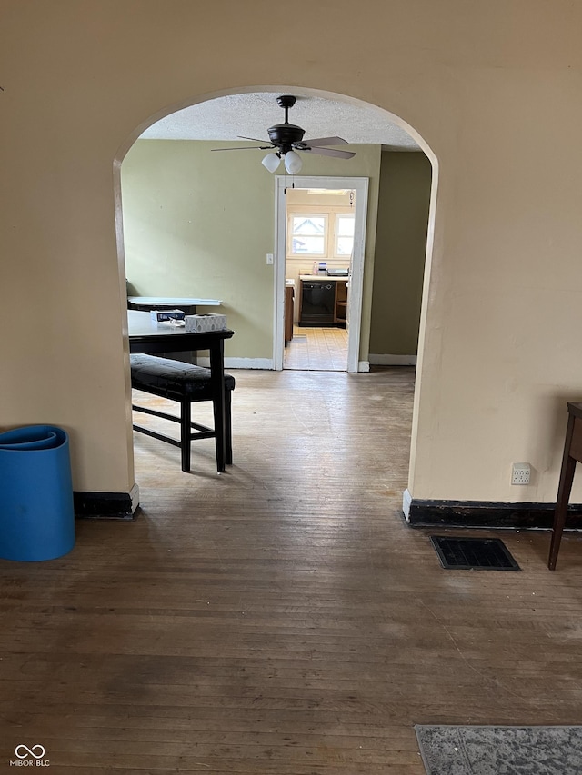 corridor with arched walkways, visible vents, baseboards, and wood finished floors