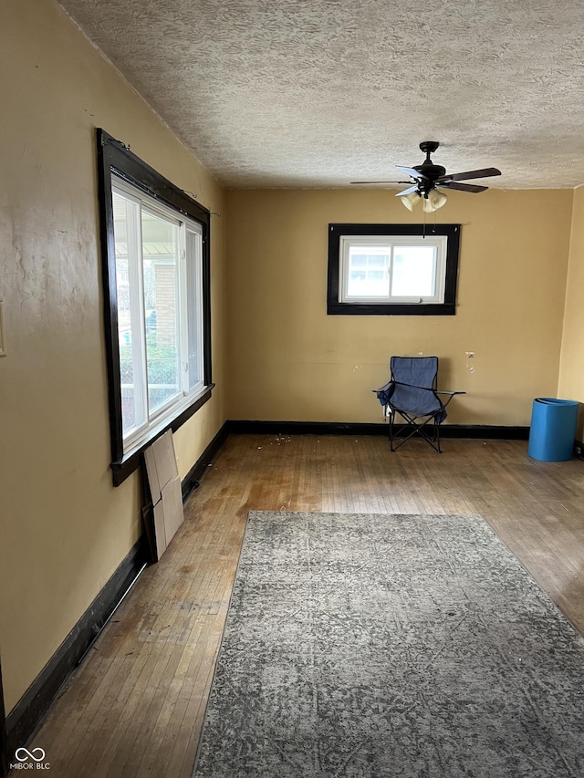 unfurnished room featuring wood-type flooring, a healthy amount of sunlight, a textured ceiling, and baseboards