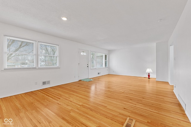 unfurnished living room featuring light wood-type flooring, visible vents, and a textured ceiling