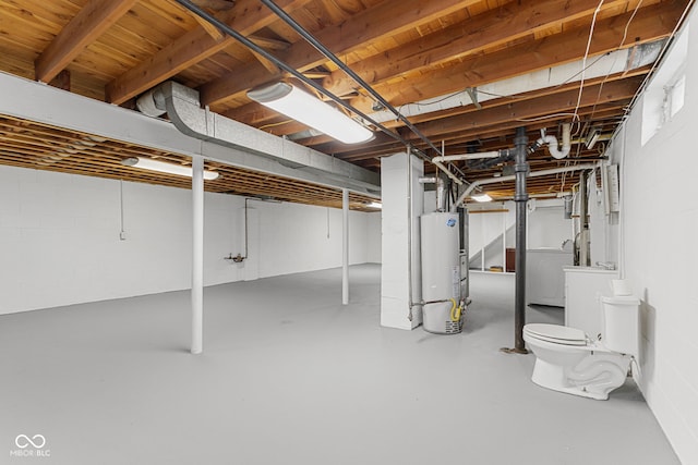 unfinished basement featuring concrete block wall, washer / dryer, and gas water heater