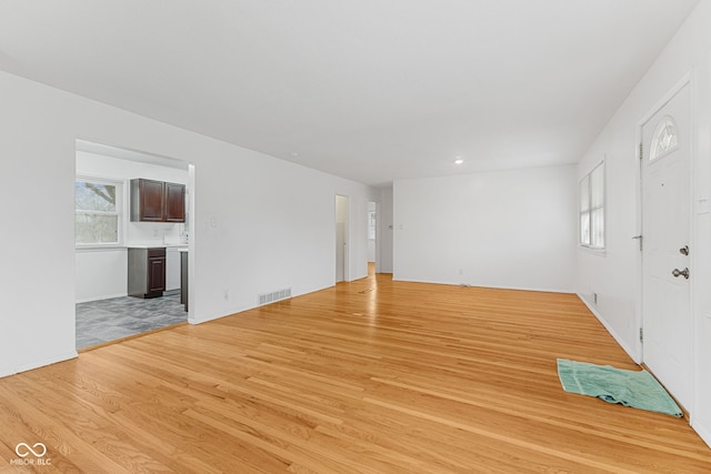 unfurnished living room featuring light wood finished floors, visible vents, and a wealth of natural light