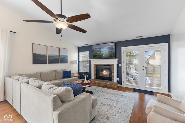 living room with visible vents, a brick fireplace, lofted ceiling, light wood-style floors, and a ceiling fan