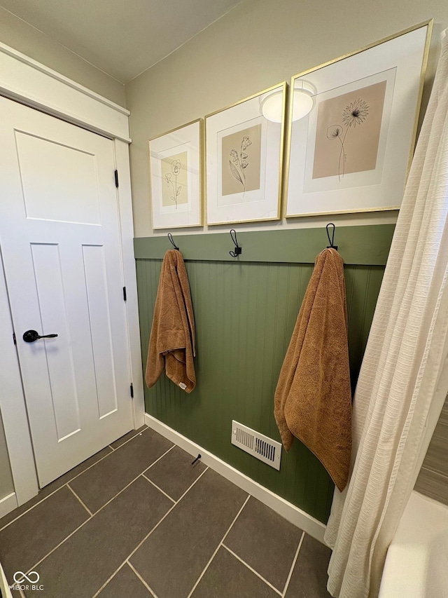 mudroom with dark tile patterned flooring, a wainscoted wall, and visible vents