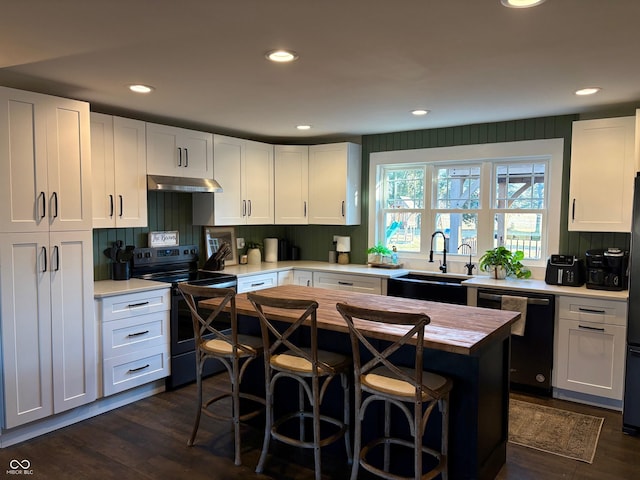 kitchen featuring dishwashing machine, under cabinet range hood, butcher block countertops, a sink, and black electric range oven