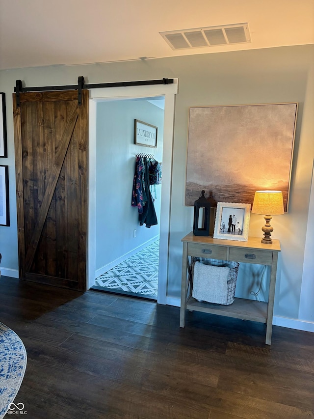 hall featuring wood finished floors, visible vents, baseboards, and a barn door