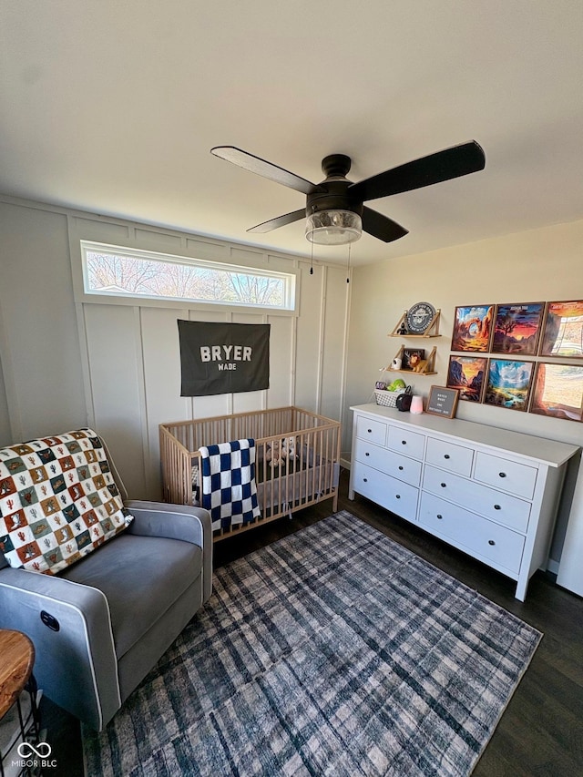 bedroom featuring ceiling fan, a crib, and dark wood-style flooring