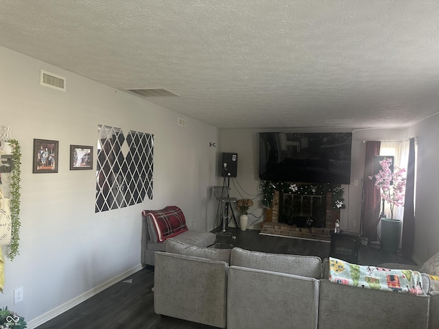 living area with baseboards, visible vents, dark wood finished floors, a textured ceiling, and a fireplace