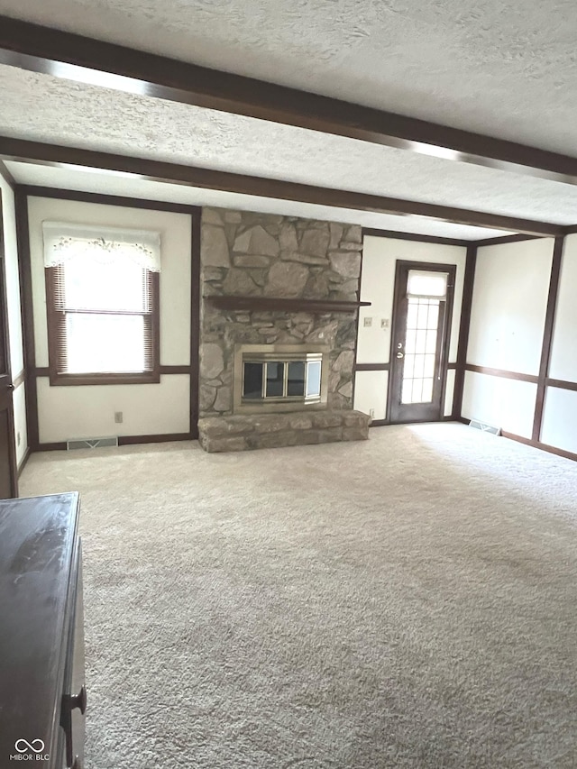 unfurnished living room with a wealth of natural light, a stone fireplace, beamed ceiling, and a textured ceiling