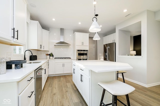 kitchen with a breakfast bar area, stainless steel appliances, a sink, visible vents, and wall chimney exhaust hood