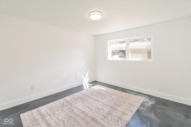 spare room featuring finished concrete floors and baseboards