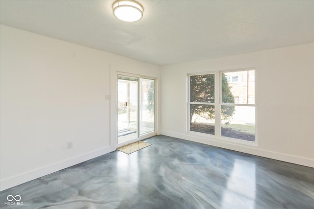 spare room featuring concrete floors, a textured ceiling, and baseboards