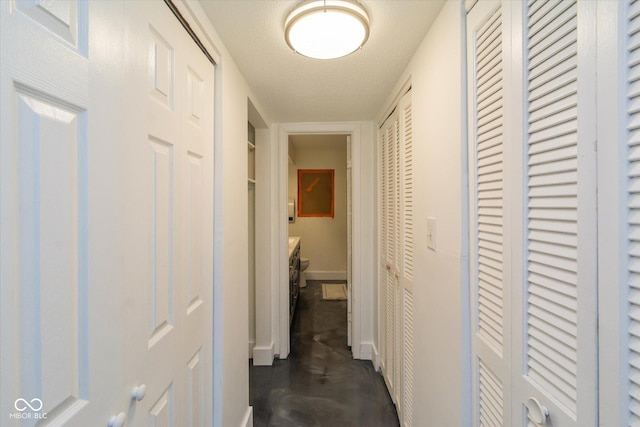 corridor with concrete floors, a textured ceiling, and baseboards