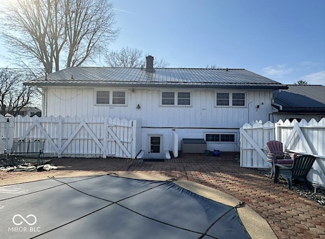 back of property with metal roof, a patio, a chimney, and fence