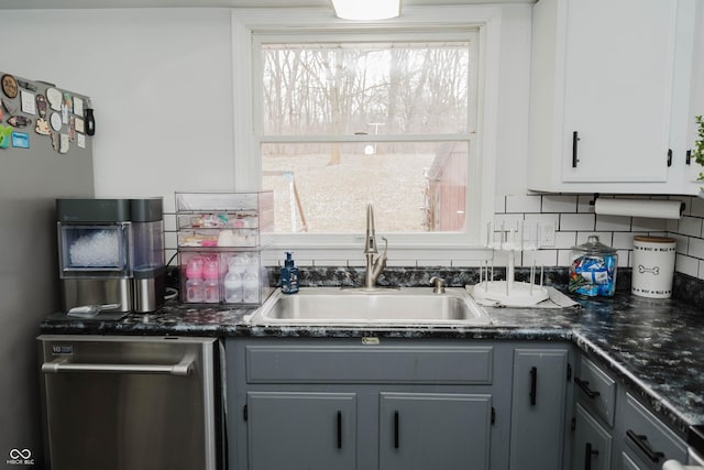 kitchen with tasteful backsplash, dark countertops, gray cabinetry, a sink, and dishwasher