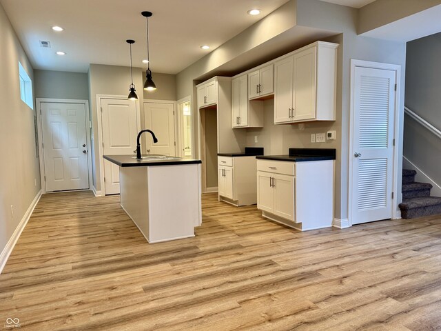 857 N Oakland Ave, Indianapolis, IN 46201 - kitchen featuring a sink, dark countertops, light wood-type flooring, a kitchen island with sink, and white cabinetry