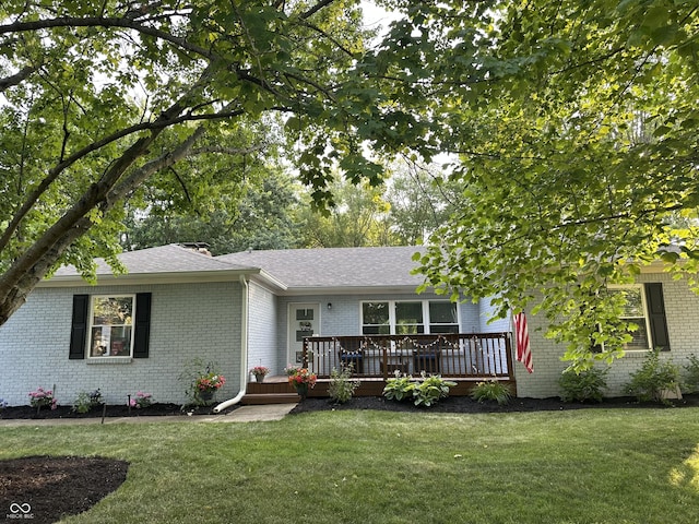 single story home with a wooden deck, roof with shingles, a front lawn, and brick siding