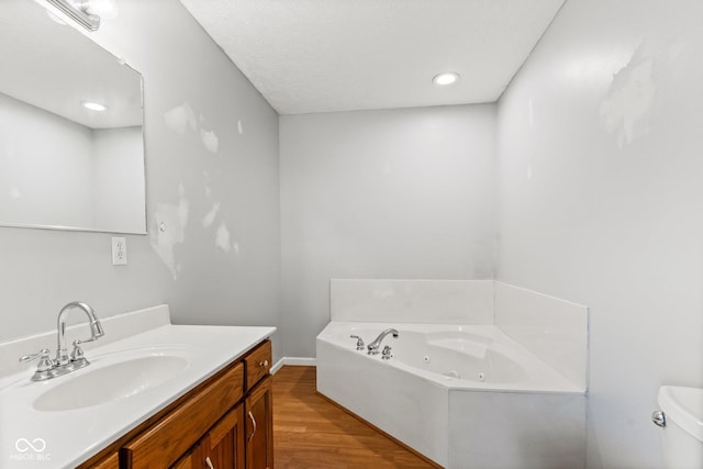 full bath with toilet, a jetted tub, wood finished floors, and vanity