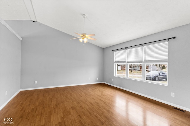 empty room with baseboards, visible vents, vaulted ceiling, and wood finished floors