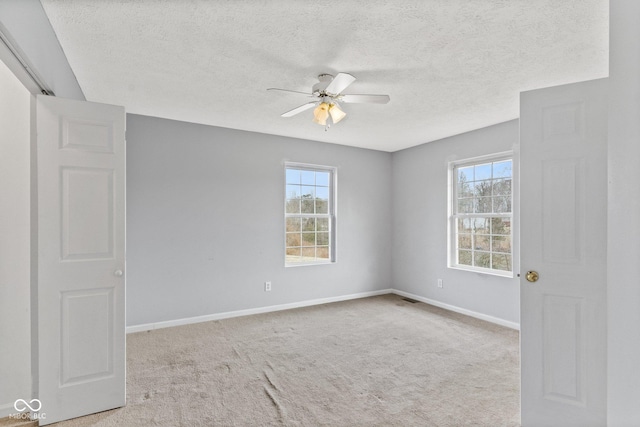 carpeted empty room featuring baseboards, a textured ceiling, a ceiling fan, and a wealth of natural light