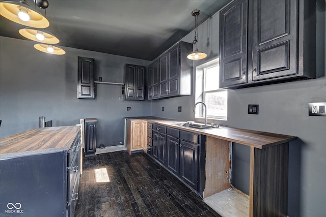 kitchen with a sink, wooden counters, hanging light fixtures, dark cabinetry, and dark wood-style floors